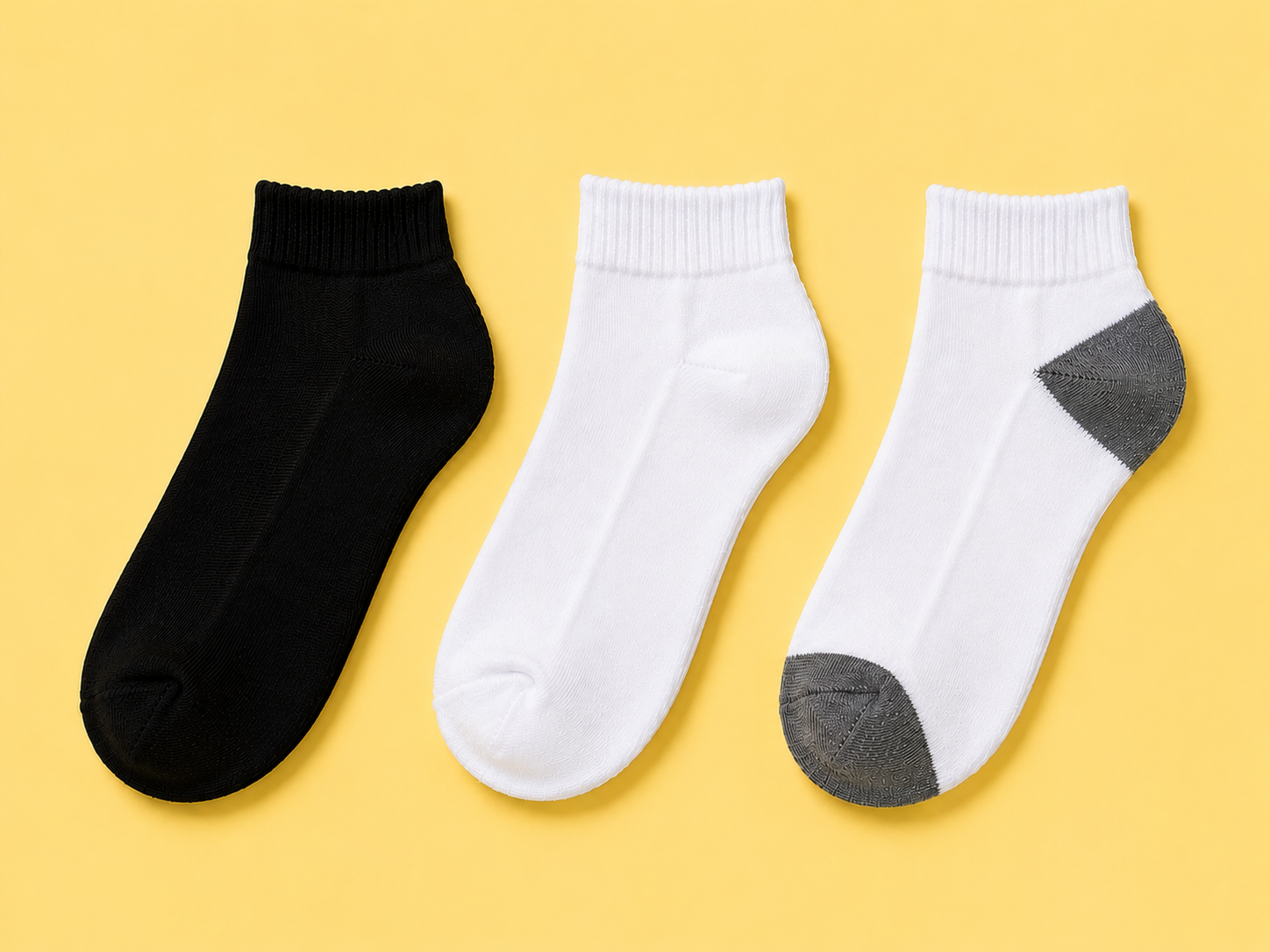 Skyland ankle socks in black, white, and white with gray heel and toe laid flat on a yellow background